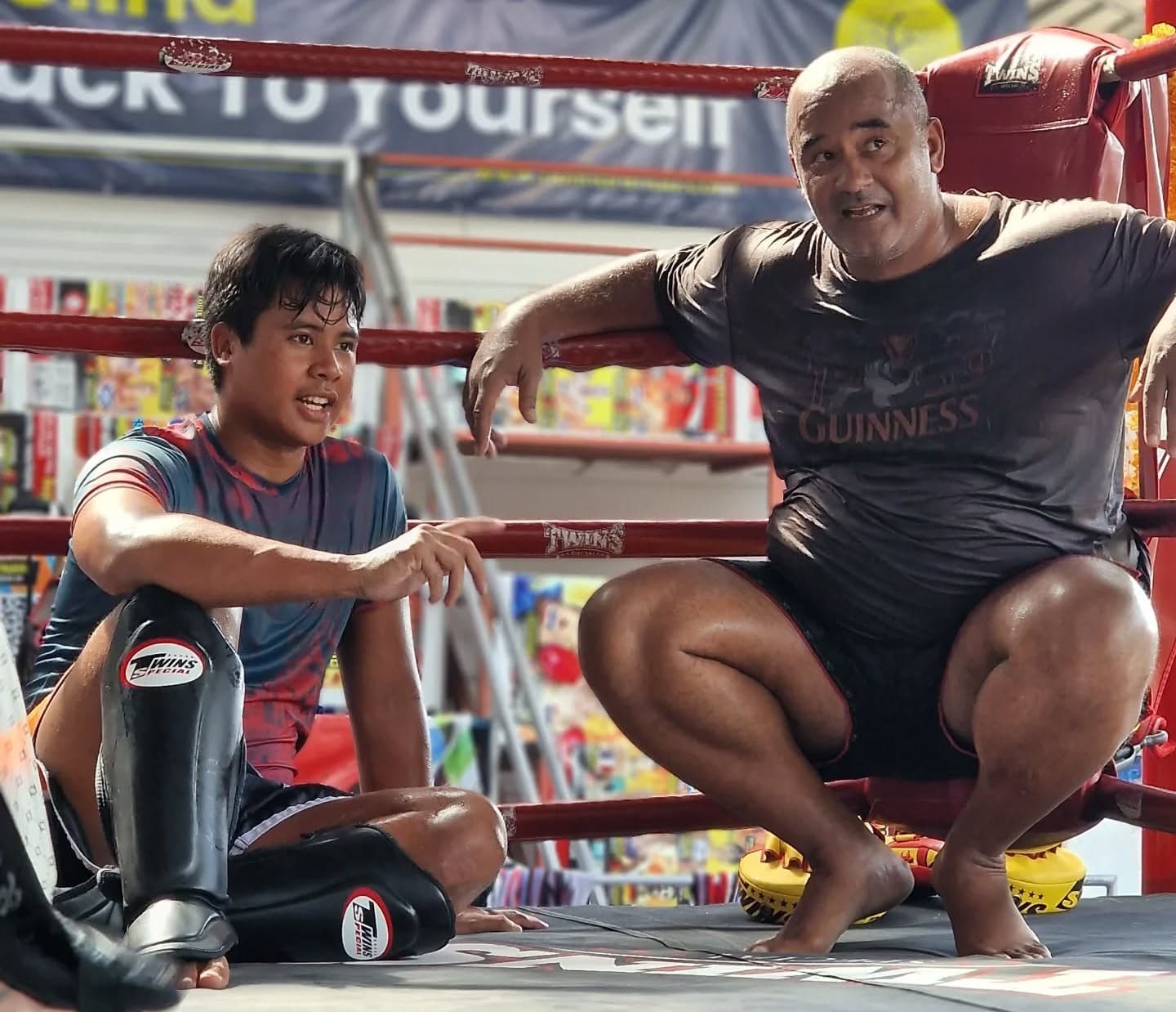 A Thai trainer and a fighter in shin guards talking in the ring at a Koh Phangan gym
