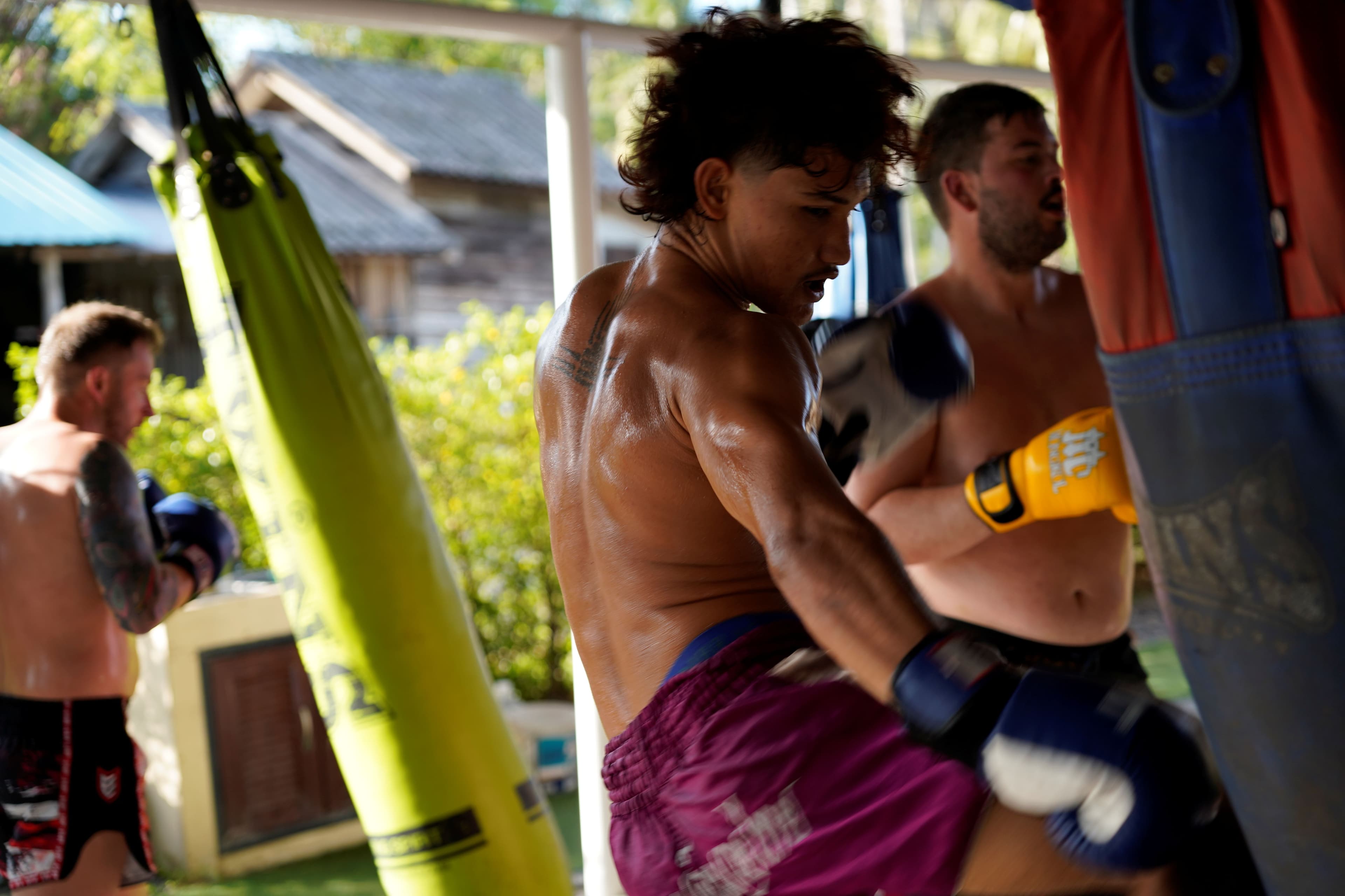 A fighter punching a heavy bag while others train around him at an open-air gym