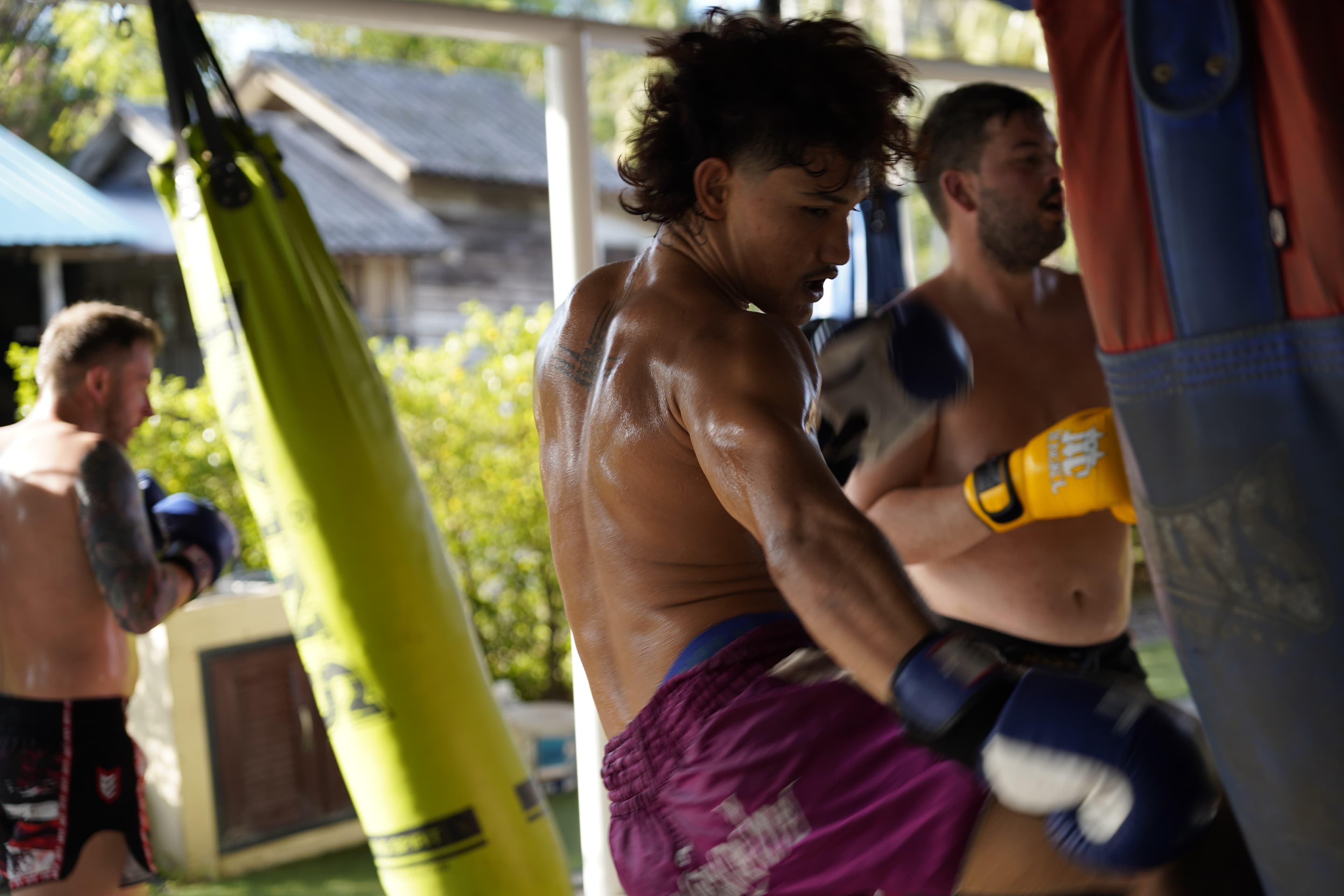 A fighter punching a heavy bag while others train around him at an open-air gym